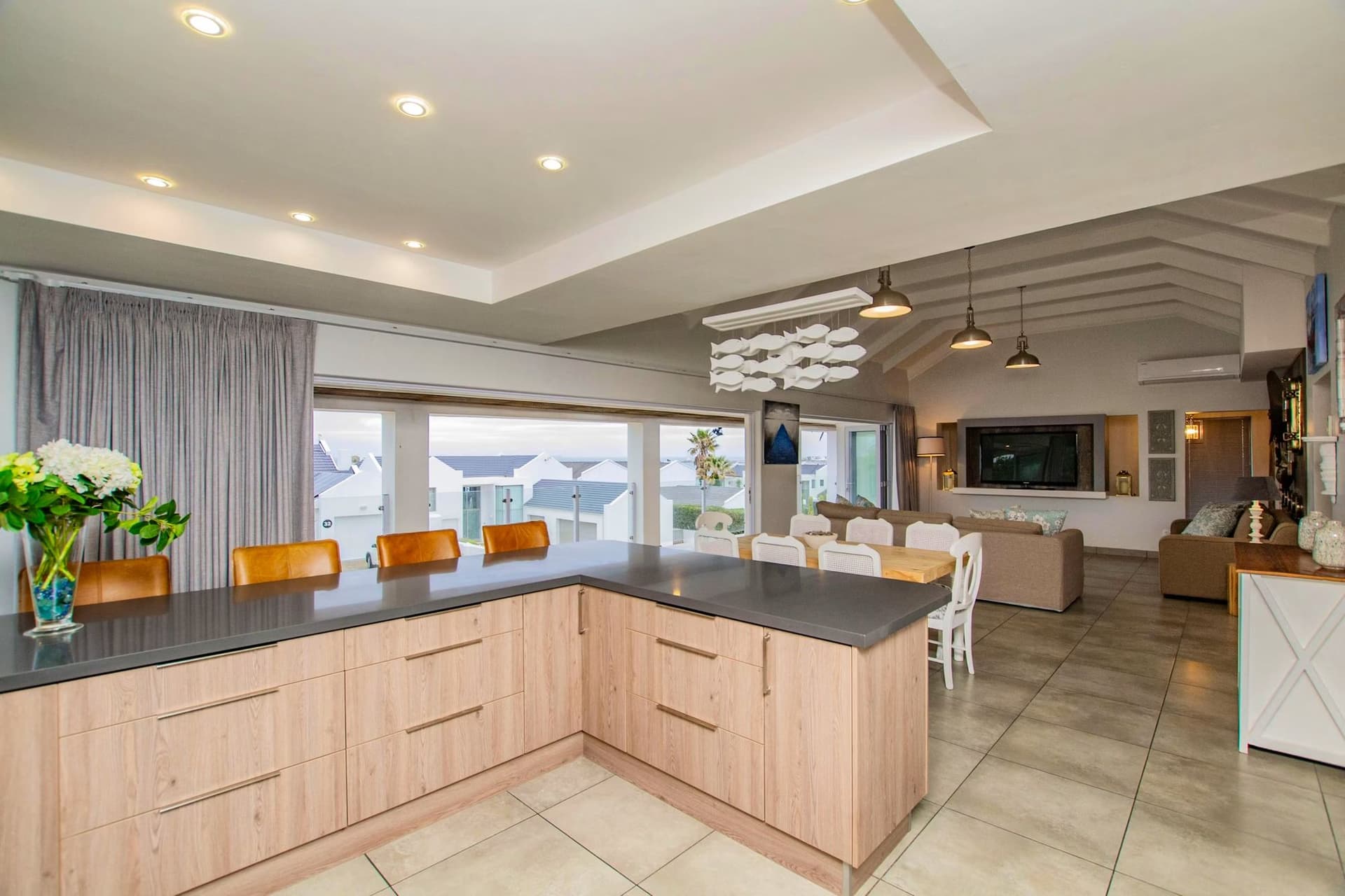 A dark-countered kitchen with timber cabinetry, open to the dining and living areas