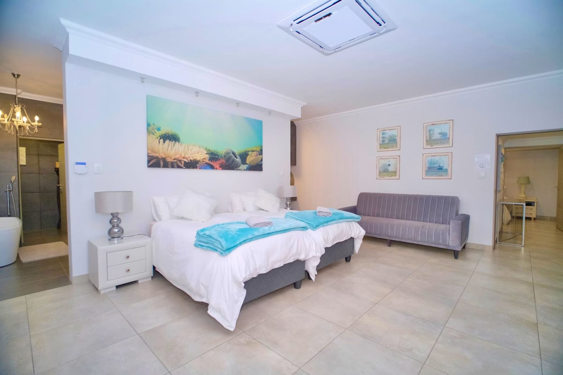 A king bedroom in teal and white linens with a sofa and wall-mounted TV