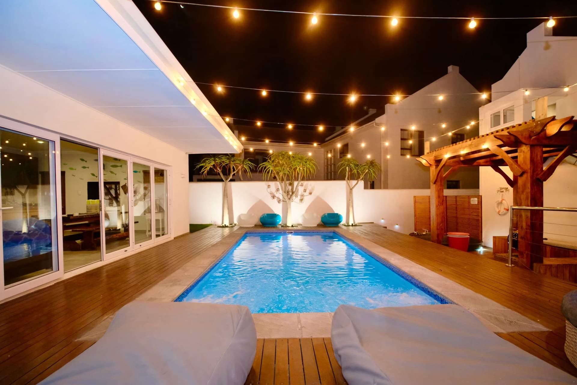 The pool and boma strung with festoon lights at night, loungers in the foreground