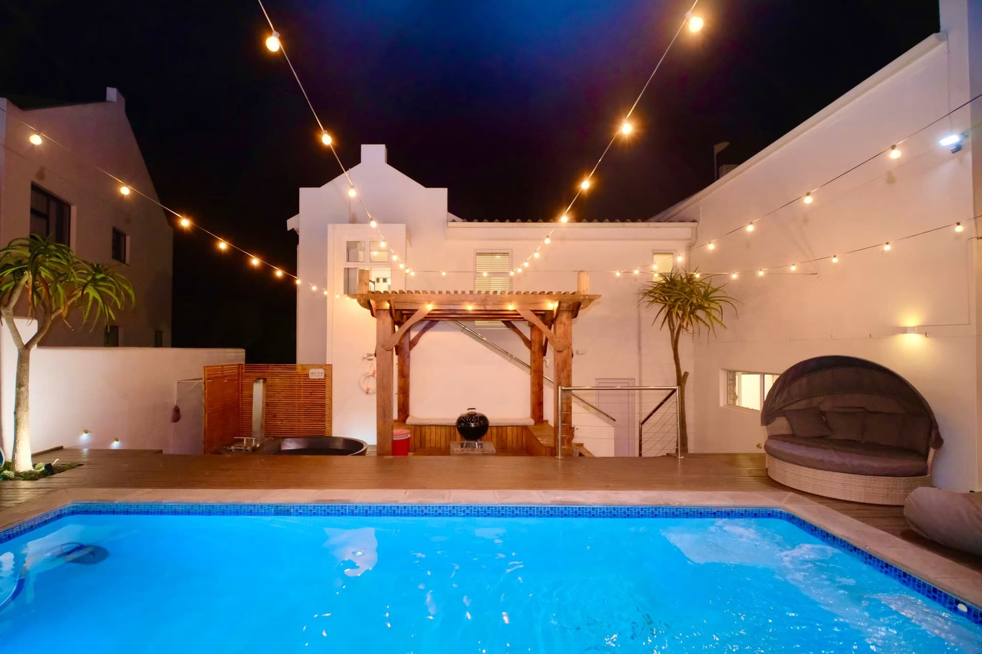 A timber boma strung with festoon lights beside the pool at night