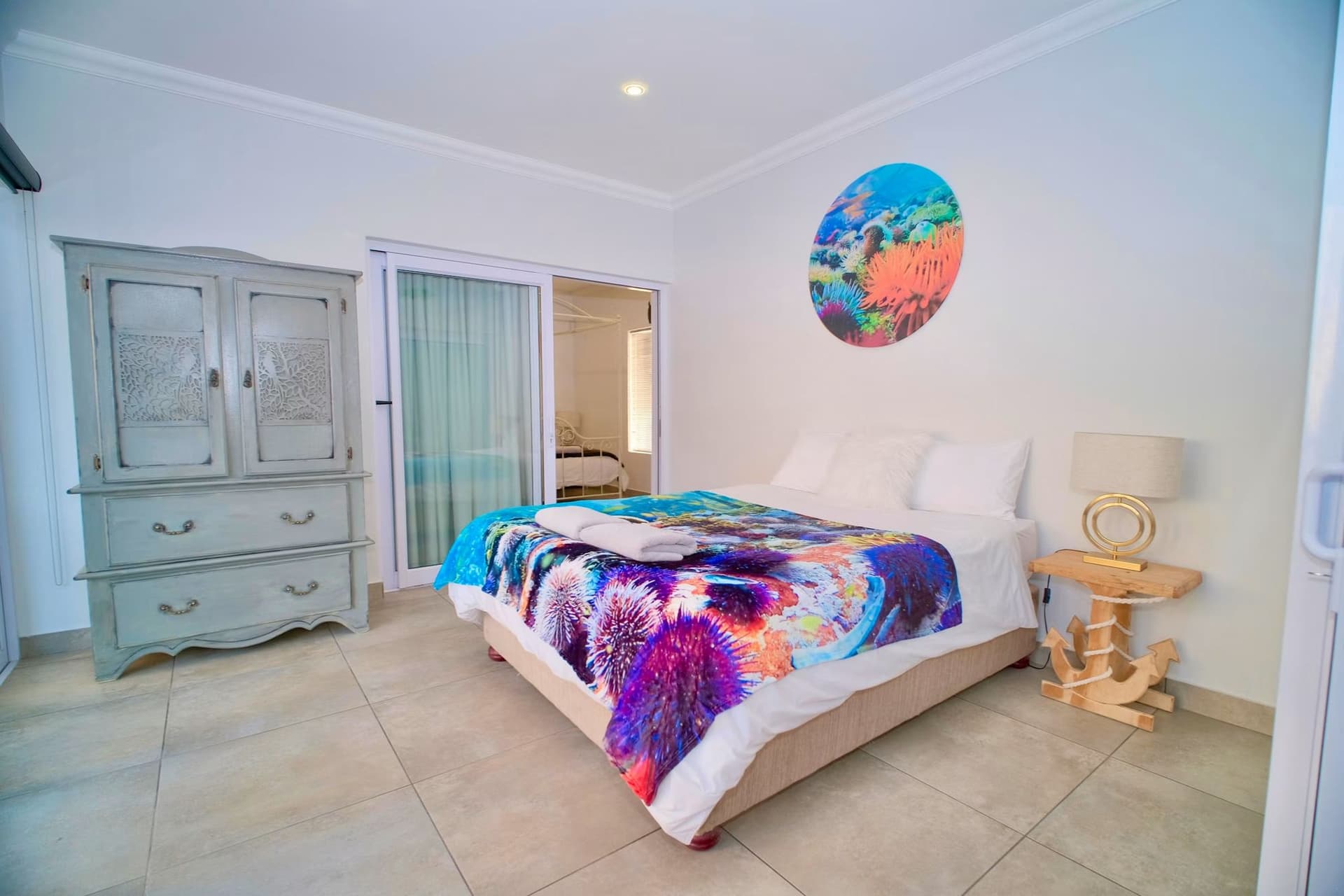 A queen bedroom dressed with a reef-print bedspread and a round reef artwork above the bed